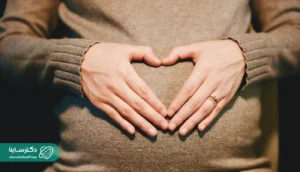 A close-up of a pregnant woman gently holding her belly in a heart shape, symbolizing care and emotional connection during hematoma in pregnancy.
