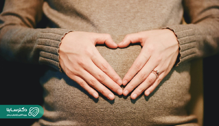 A close-up of a pregnant woman gently holding her belly in a heart shape, symbolizing care and emotional connection during hematoma in pregnancy.